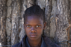 Young girl with serious look leaning against tree, Botswana