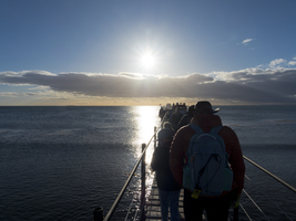 Reisegruppe auf Bootssteg bei Sonnenaufgang über dem Meer an der Magellanstraße, Punta Arenas, Chile