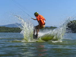 Junger lässiger Mann mit flatternden Hemd auf Wakeboard bei Sprung in den See, Wasserski und Wakepark, Stráž pod Ralskem, Tschechien