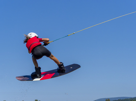 Junge oder Mädchen, Sprung mit Wakeboard über den See, rote Schwimmweste und Wassersport, Wasserski im Wakepark, Stráž pod Ralskem, Tschechien