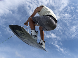 Junger Mann bei Sprung und Flug mit Wakeboard, Wassersport und Wasserski im Wakepark, Stráž pod Ralskem, Tschechien