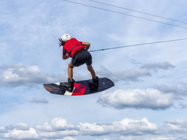 Junge oder Mädchen bei Sprung und Flug mit Wakeboard durch Wolken, Wassersport und Wasserski im Wakepark, Stráž pod Ralskem, Tschechien