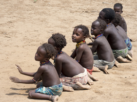 Singing happy children sit on sandy ground, Dassanech tribe, Ethiopia, Africa