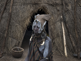 Woman from the Mursi tribe with headdress and face-paint in front of her hut, Ethiopia, Africa