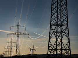 Hochspannungstrasse mit Masten und Überlandleitungen, metallisch glänzende Leitungen , Windräder am Horizont, Sachsen, Deutschland
