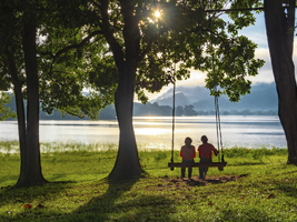 Mädchen sitzen auf Schaukel am Baum in Morgensonne am See, Sri Lanka