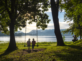 Mädchen sitzen auf Schaukel am Baum in Morgensonne am See, Sri Lanka