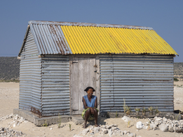 Woman sitting in front of tin hut in the village of Sarondrano, Madagascar