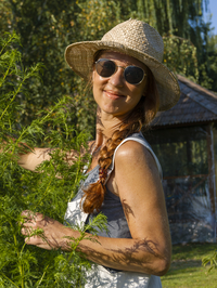 Frau in Kräuterbeet, Porträt, Heilkräuter im Garten, Gartenarbeit im Kräutergarten mit Strohhut und Sonnenbrille, Deutschland