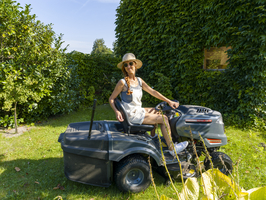 Frau fährt Rasenmäher, Rasentraktor, mit Strohhut und Sonnenbrille, im Garten bei der Arbeit, Deutschland