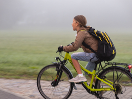 Kind, Junge fährt mit Fahrrad und Schultasche im Nebel am Wiesenrand, Deutschland